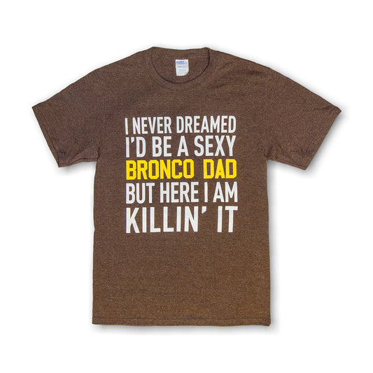 Brown t-shirt with text 'I NEVER DREAMED I'D BE A SEXY BRONCO DAD BUT HERE I AM KILLIN' IT' printed in white and yellow.
